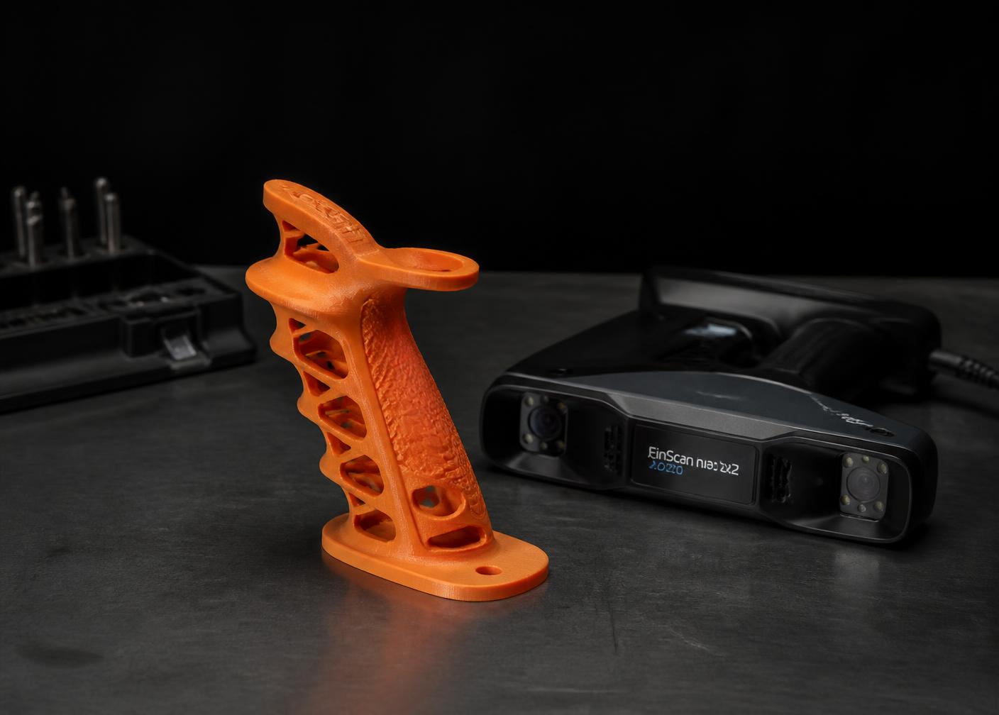 Custom orange 3D printed ergonomic sports grip beside a handheld 3D scanner